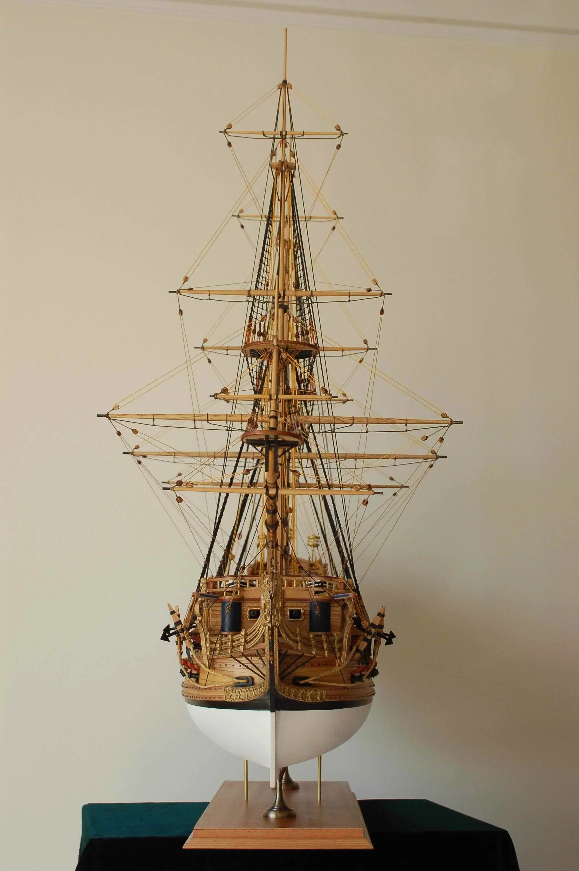 Wooden model ship on a stand against a plain wall